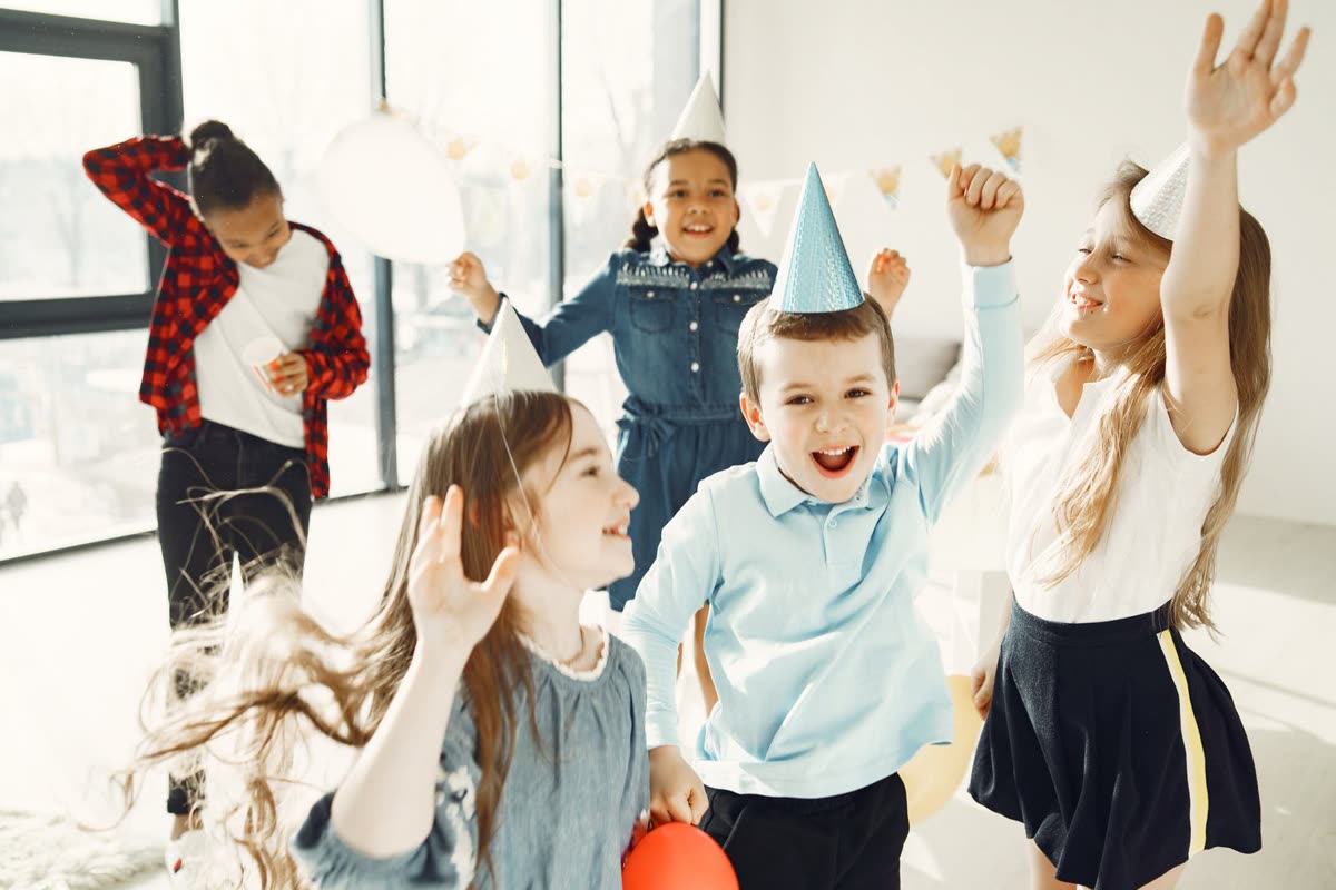 Children in party hats dancing and cheering at a birthday party