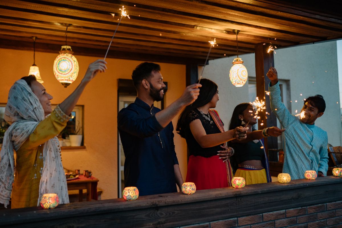 Friends in traditional Indian clothing laughing and holding sparklers on a lantern-lit terrace during a Diwali celebration
